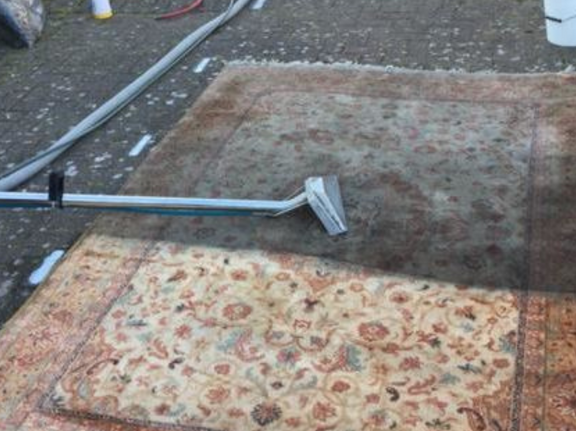 This is a photo of a floral rug that is being steam cleaned. The bottom half has been completed and the top half is being done works carried out by Borehamwood Carpet Cleaning