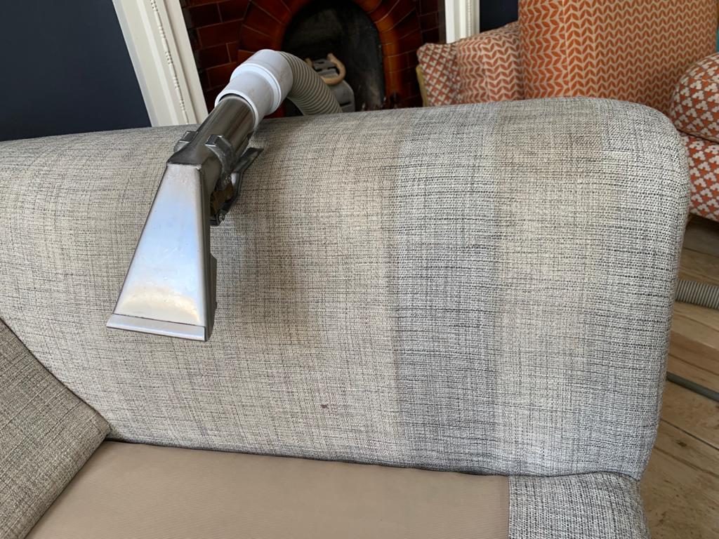 This is a photo of an arm of beige sofa that shows a test patch that has been steam cleaned. The steam cleaning machine is also showing in the photo works carried out by Borehamwood Carpet Cleaning