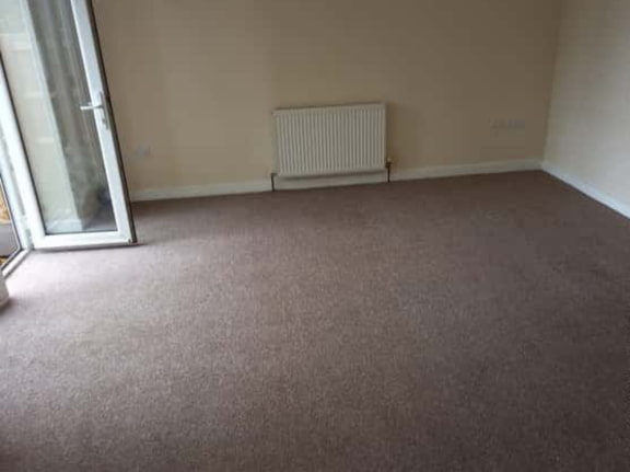 This is a photo of a living room after it has been cleaned. The room is empty and has a brown carpet that has been steam cleaned works carried out by Borehamwood Carpet Cleaning